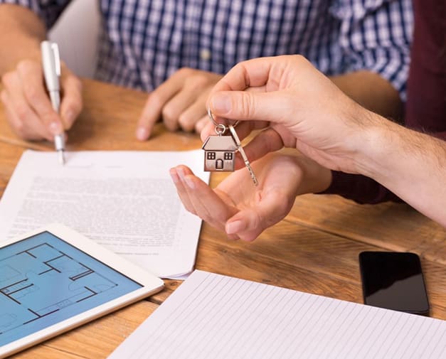 Two people are holding keys to a house.